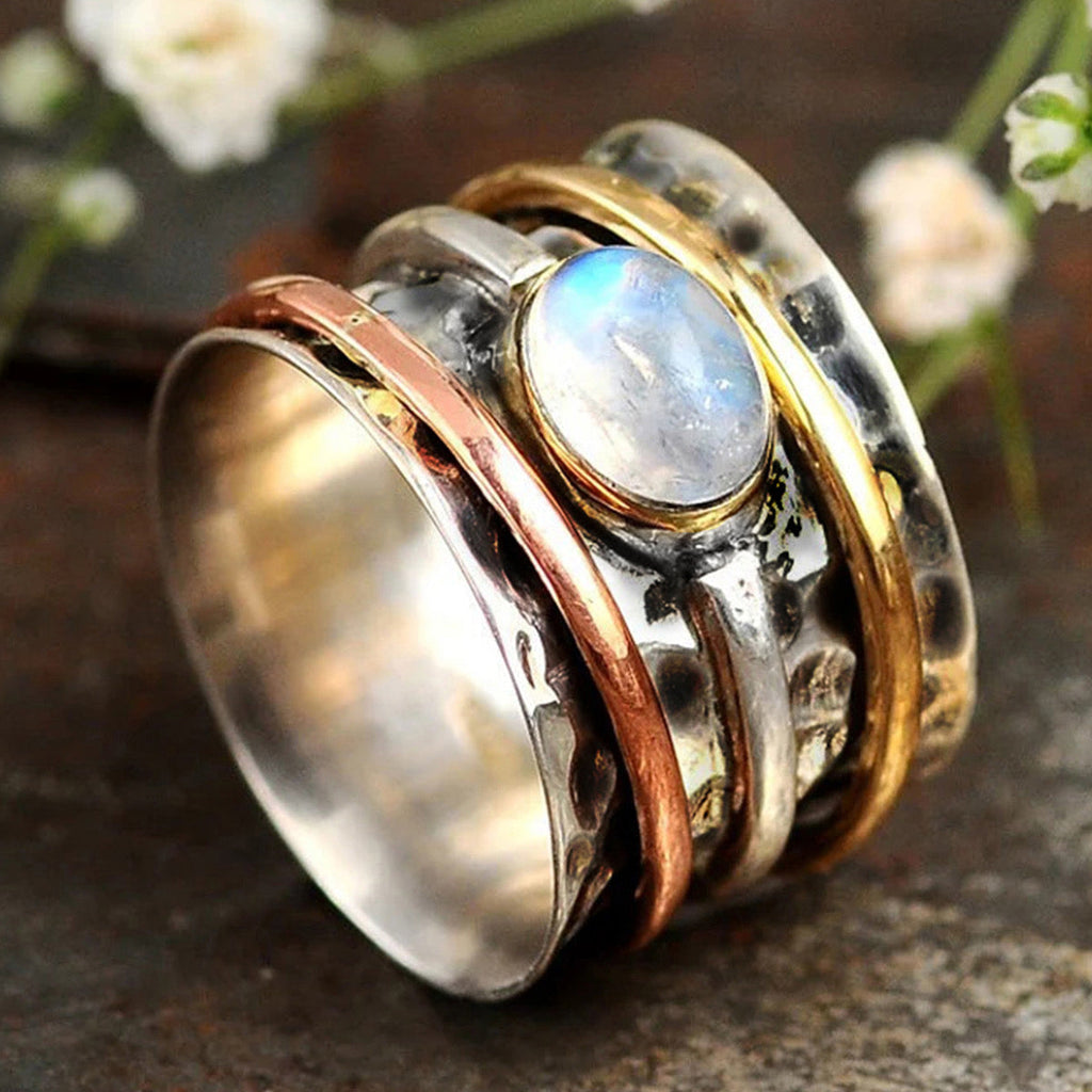 Moonstone tri-tone spinner ring on dark stone surface with white flowers
