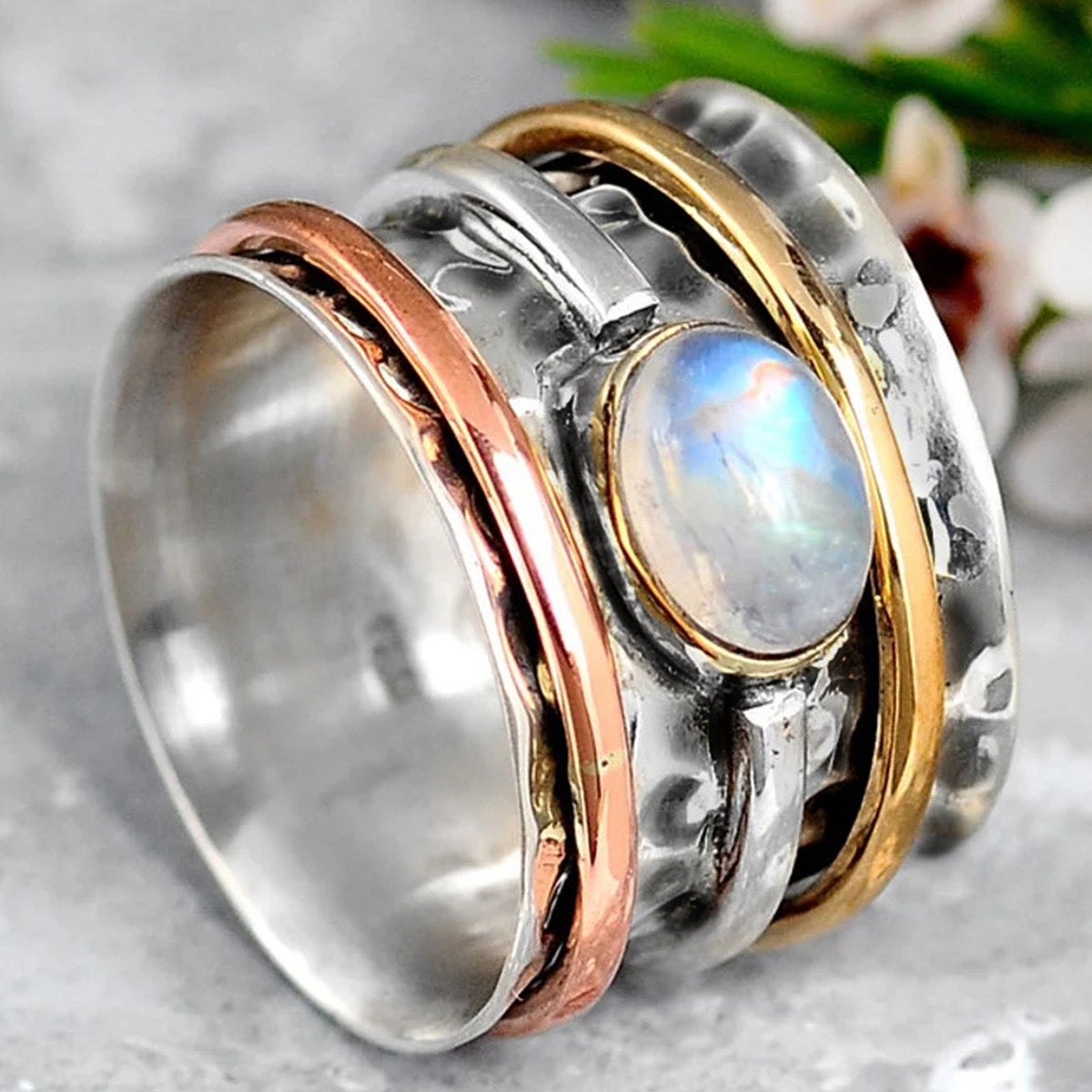 Moonstone tri-tone spinner ring on grey marble surface with botanicals